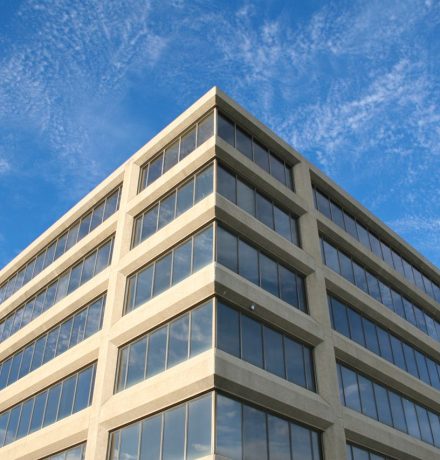 Corner view of a modern office building with reflective windows under a clear blue sky.